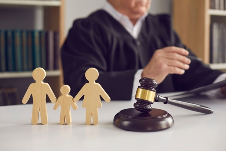 Gavel, sound block and small wooden figurines of husband, wife and kid on judge's table in courthouse